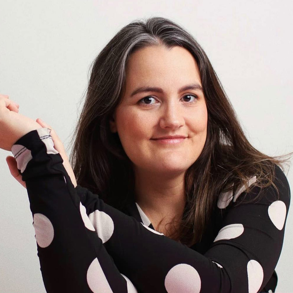 Portrait of Luiza, sidekick mentor, white woman, long dark hair, black shirt with large white dots, smilling.