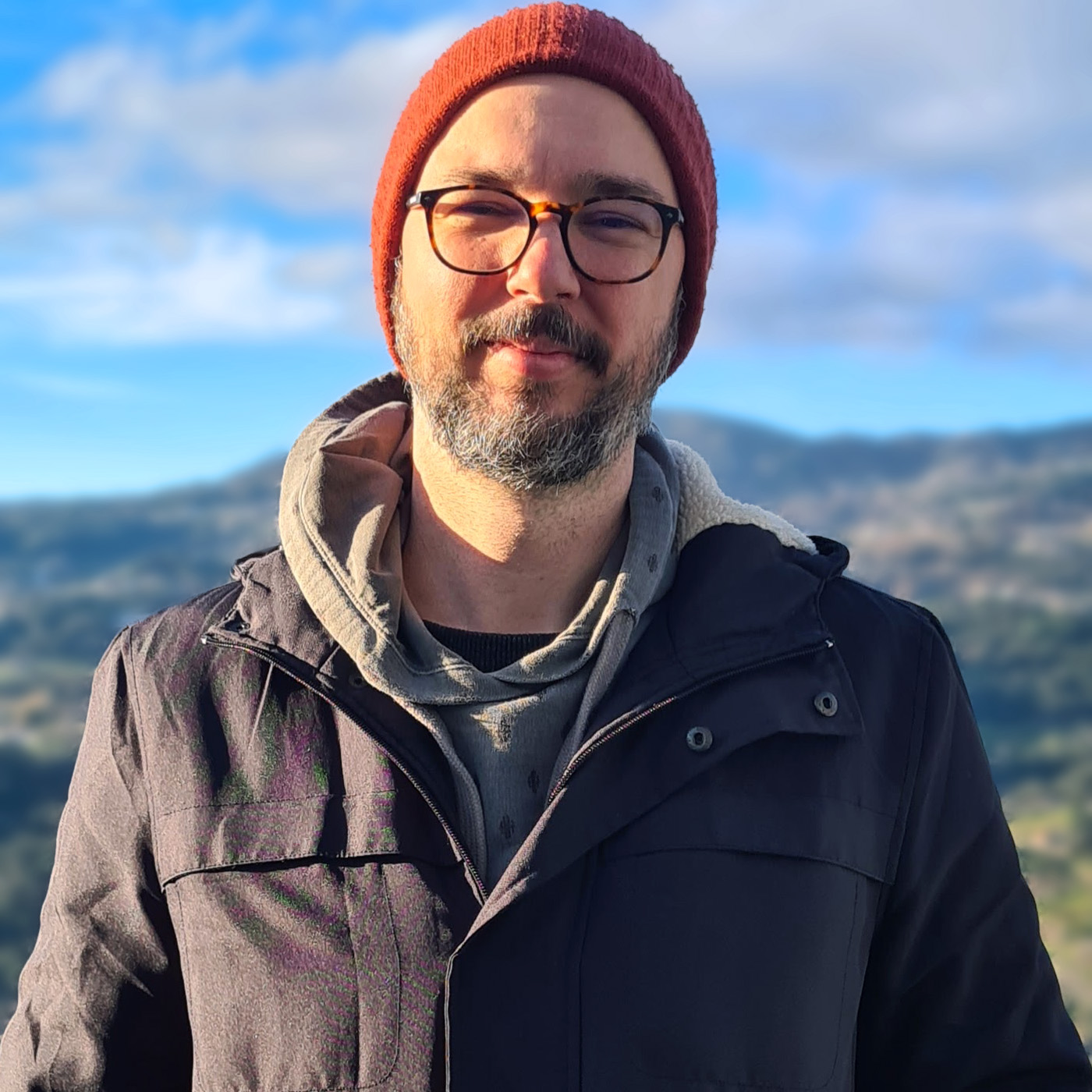 Portrait of Victor, sidekick mentor, white man, wearing winter clothes and a red beanie, glasses, smilling.